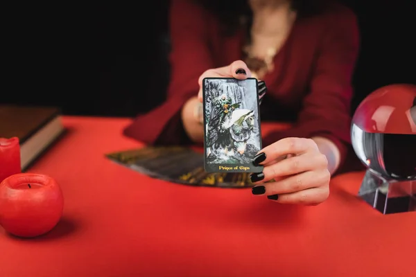 KYIV, UKRAINE - FEBRUARY 23, 2022: Cropped view of blurred soothsayer showing tarot card near orb and candles — стокове фото