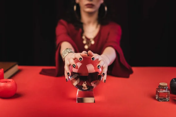 Cropped view of blurred soothsayer touching magic orb isolated on black - foto de stock