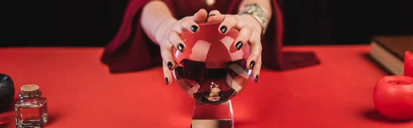 Cropped view of medium touching glass orb near candles isolated on black, banner — Fotografia de Stock