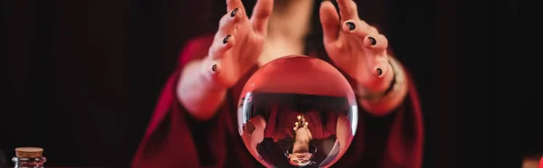 Cropped view of blurred soothsayer and magic orb isolated on black, banner — Stock Photo