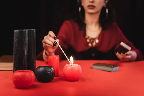 Cropped view of blurred medium burning candle and holding tarot cards isolated on black - foto de stock