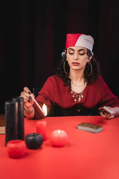 Zigeuner-Wahrsager gräbt verschwommene Kerzen und hält Tarot isoliert auf schwarz — Stockfoto
