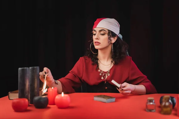 Gypsy medium burning candle near tarot and book on table isolated on black — Stock Photo