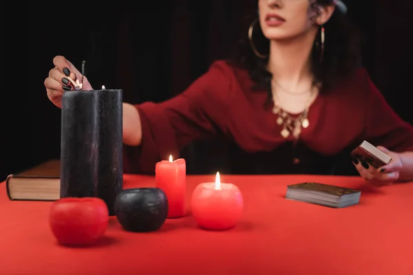 Cropped view of medium burning candles near tarot cards isolated on black - foto de stock