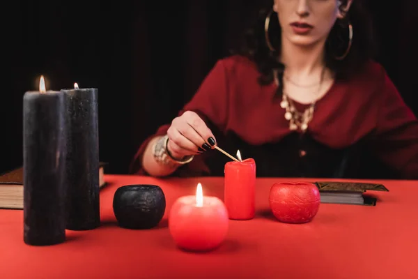 Cropped view of blurred soothsayer burning candles near book and tarot isolated on black — Stock Photo