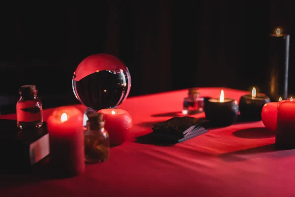 Velas encendidas borrosas cerca de orbe mágico y cartas del tarot aisladas en negro - foto de stock