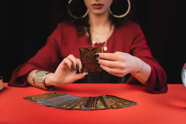 KYIV, UKRAINE - FEBRUARY 23, 2022: Cropped view of blurred witch holding tarot card isolated on black — стоковое фото