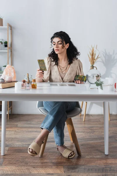 Zigeuner-Wahrsagerin hält verschwommene Tarotkarten in der Nähe von Hexereivorräten auf dem Tisch — Stockfoto