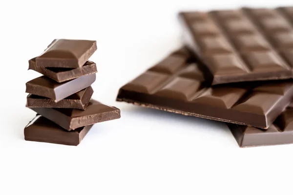 Close up view of pieces of dark chocolate near blurred bars on white background — Stock Photo