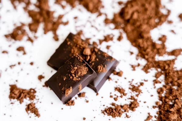 Vista de cerca de piezas de chocolate con cacao seco sobre fondo blanco - foto de stock
