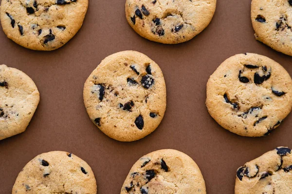 Draufsicht auf Kekse mit Schokoladenstücken auf braunem Hintergrund — Stockfoto