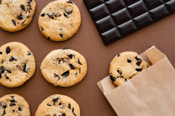 Top view of cookies, paper bag and chocolate bar on brown background — стоковое фото