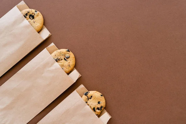 Vue du dessus des cookies dans les emballages artisanaux sur fond marron avec espace de copie — Photo de stock