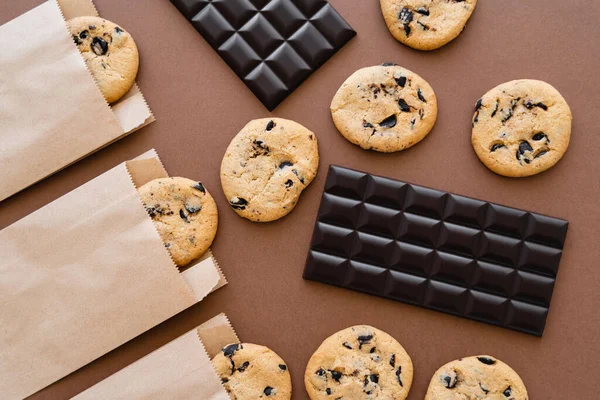 Vue du dessus des barres de chocolat et des biscuits dans des emballages artisanaux sur fond brun — Photo de stock