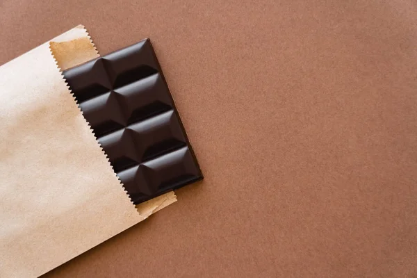 Vista superior de la barra de chocolate negro en paquete de artesanía sobre fondo marrón - foto de stock