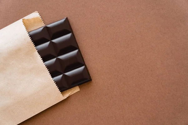 Top view of dark chocolate bar in craft package on brown background — Stock Photo