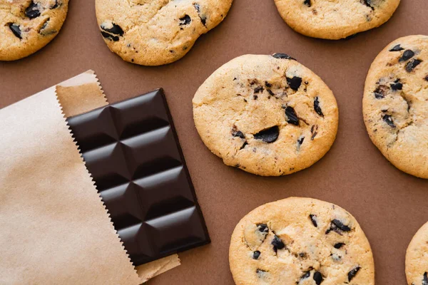 Top view of cookies near chocolate bar in craft package on brown background — Stock Photo