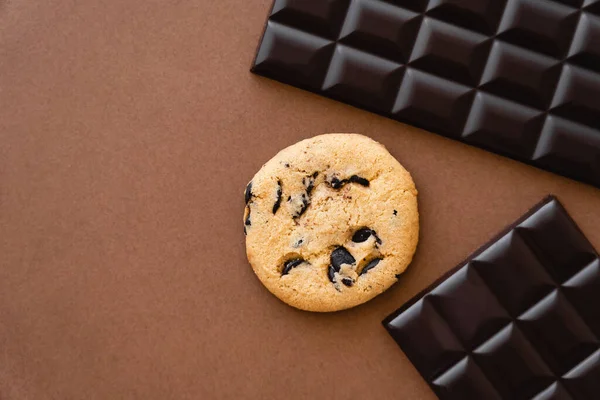 Vista superior de la galleta cerca de las barras de chocolate oscuro sobre fondo marrón - foto de stock