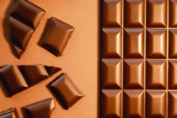 Top view of milk chocolate bar and pieces on brown background — Stock Photo