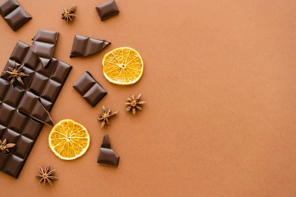 Top view of dark chocolate, dry orange slices and anise spice on brown background — Photo de stock