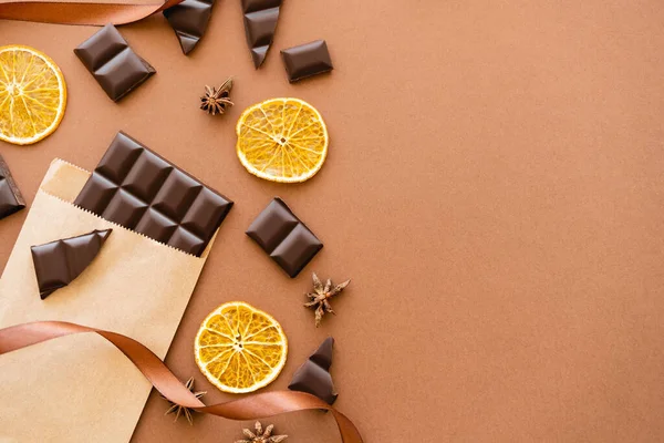 Vista superior de chocolate no pacote de artesanato, fatias de laranja e anis no fundo marrom — Fotografia de Stock