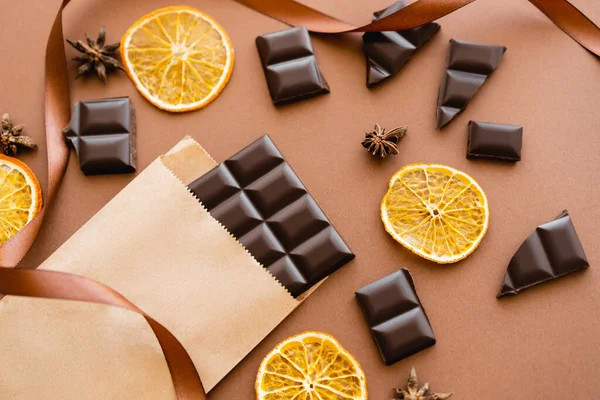 Top view of anise, dry orange slices and chocolate on craft package with ribbon on brown background — Fotografia de Stock