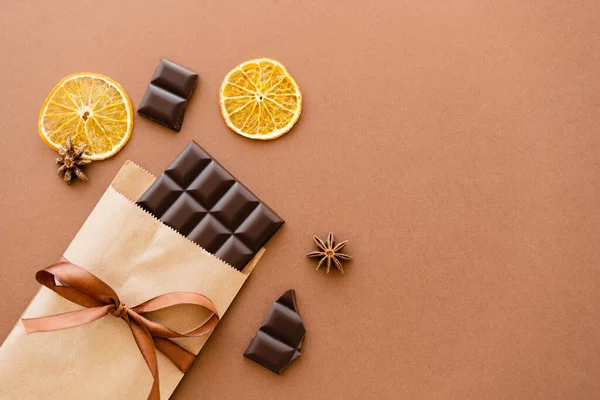 Vista superior de anis e fatias de laranja perto de chocolate no pacote de artesanato com fita no fundo marrom — Fotografia de Stock