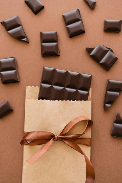 Top view of dark chocolate in craft package with ribbon on brown background — Photo de stock