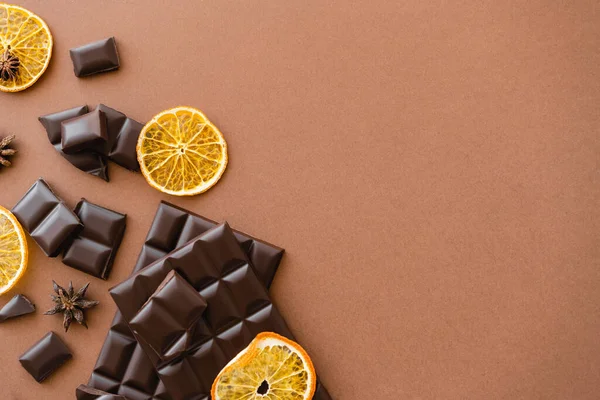 Vue de dessus des barres de chocolat noir près des tranches d'orange sèches et de l'anis sur fond brun — Photo de stock