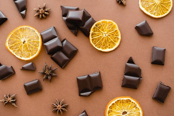 Vue du dessus des morceaux de chocolat, des tranches d'orange sèche et de l'anis sur fond brun — Photo de stock