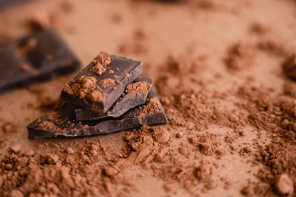 Vue rapprochée de la poudre de cacao naturelle et du chocolat sur fond brun flou — Photo de stock