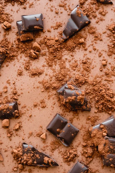 Draufsicht auf trockenen Kakao und dunkle Schokoladenstücke auf braunem Hintergrund — Stockfoto