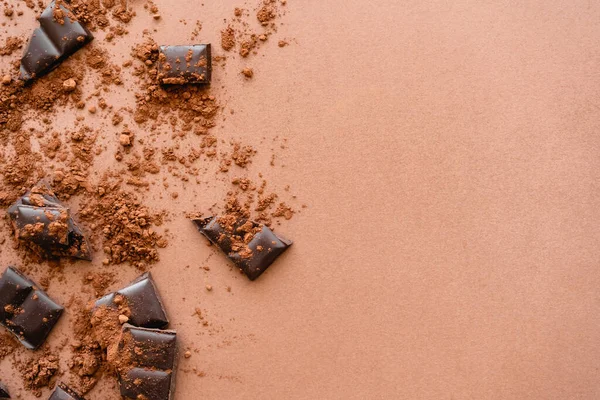 Top view of chocolate pieces and cocoa on brown background with copy space — Stock Photo