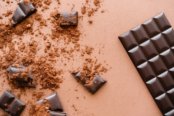 Top view of chocolate bar near pieces and dry cocoa on brown background — стоковое фото