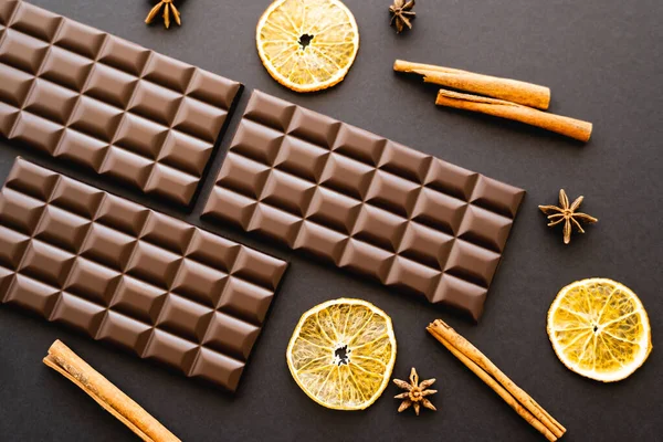 Top view of chocolate bars, spices and dry orange slices on black background - foto de stock