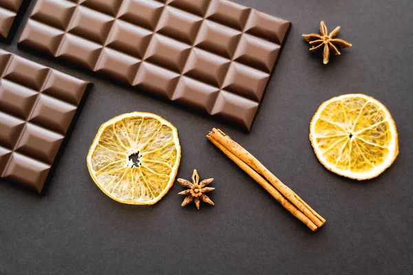 Vista dall'alto di fette di arancia secca, spezie e barrette di cioccolato su sfondo nero — Foto stock