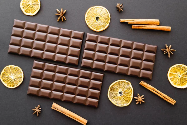 Vista dall'alto di barrette di cioccolato, arancia secca e spezie su sfondo nero — Foto stock