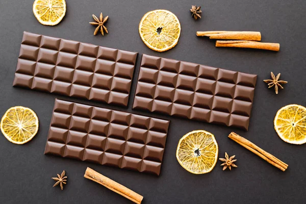 Top view of chocolate bars, dry orange and spices on black background — Stock Photo