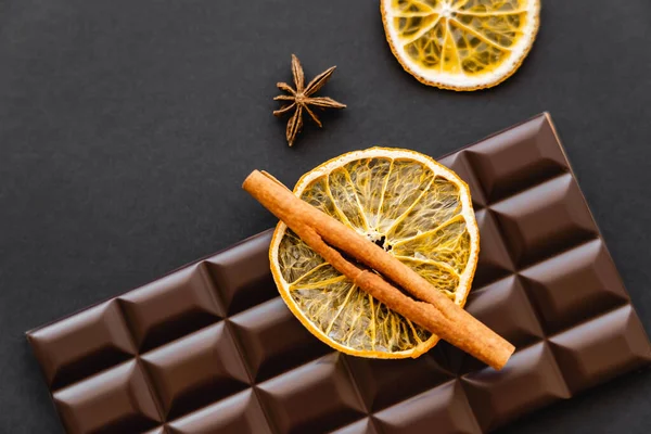 Top view of cinnamon on dry orange slice and chocolate bar on black background - foto de stock