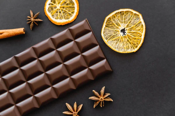 Top view of chocolate bar near dry orange slices and anise on black background — Fotografia de Stock