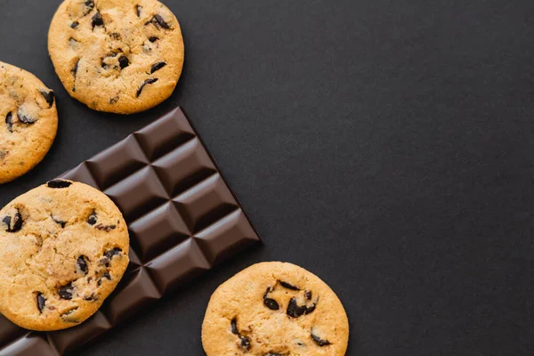 Vue du dessus des biscuits et de la barre de chocolat sur la surface noire — Photo de stock