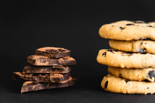 Vue rapprochée des morceaux de chocolat au cacao près des cookies sur fond noir — Photo de stock