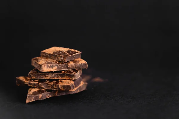 Vue rapprochée de morceaux de chocolat noir avec cacao sec sur surface noire — Photo de stock