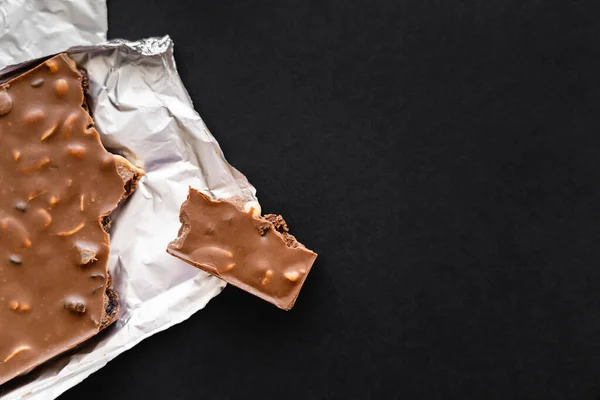 Top view of milk chocolate with nuts on foil on black background — Stockfoto