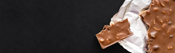 Top view of milk chocolate with nuts on foil on black background, banner — Fotografia de Stock