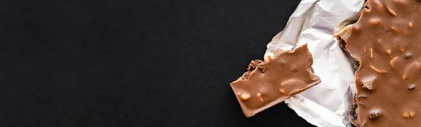 Top view of milk chocolate with nuts on foil on black background, banner — Stock Photo