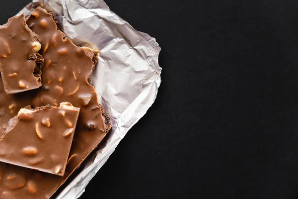 Top view of natural milk chocolate with nuts on foil isolated on black — Stock Photo