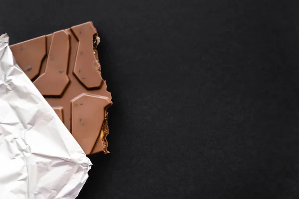 Top view of milk chocolate in foil on black background with copy space — Stock Photo