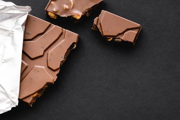 Top view of delicious milk chocolate with nuts in foil on black background — Stock Photo