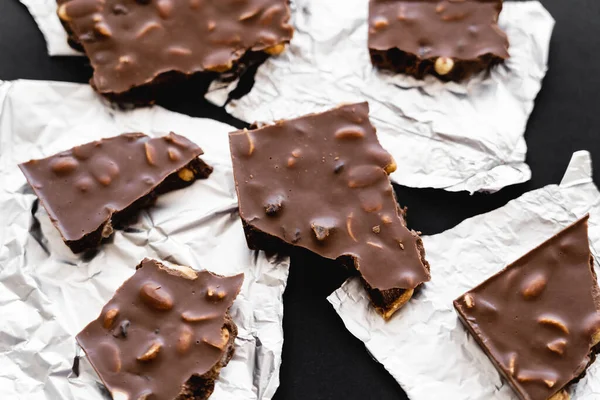 Top view of milk chocolate with nuts on foil on black background — стоковое фото